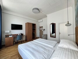 Quarto de hotel com duas camas, uma escrivaninha, uma cadeira, guarda-roupa, televisão e espelho.