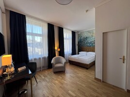 Una camera d'albergo con un letto, una scrivania con una lampada, una sedia e vista sulla città dalla finestra.
