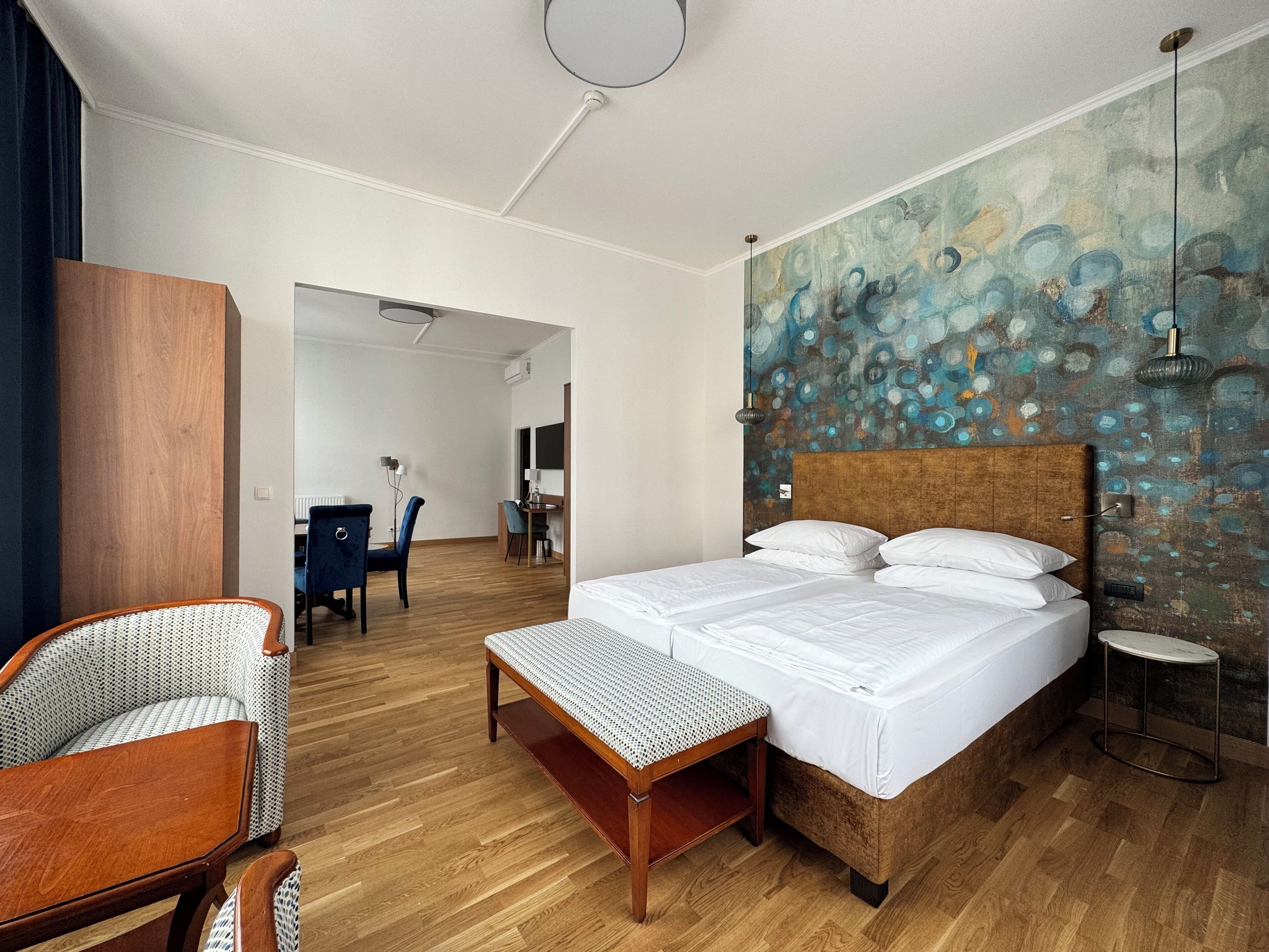 A hotel room with a large bed, a desk, a chair, and a wooden floor.