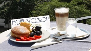 A table with a sign reading "HOTEL SECESSION," a plate with food, and a glass of beer, overlooking a cityscape with buildings and a dome. - Hotel Secession an der Oper (Vienna)