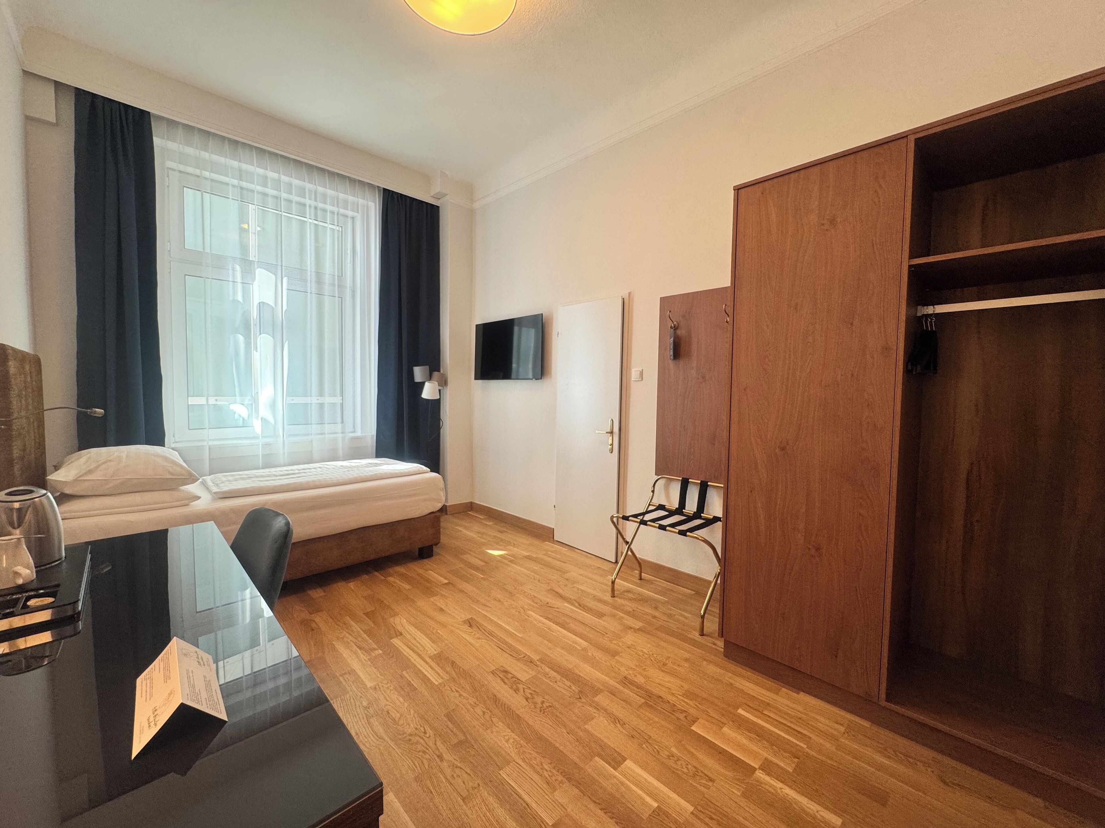 A bedroom with a bed, a desk, a TV, a wardrobe, and a window with curtains.