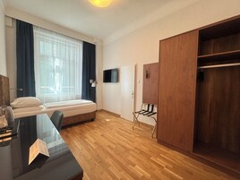 Een slaapkamer met een bed, een bureau, een televisie, een kast en een raam met gordijnen.