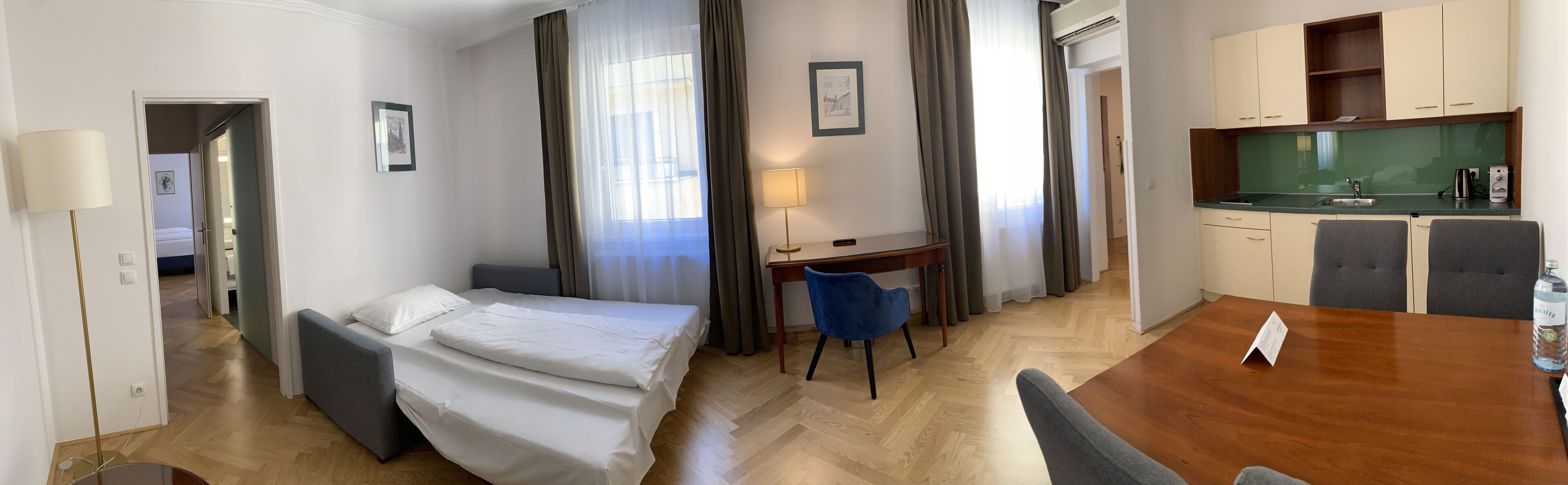 A hotel room with a bed, desk, chair, and kitchenette.