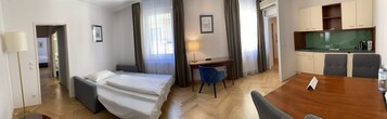 Quarto de hotel com cama, escrivaninha, cadeira e cozinha compacta.