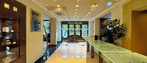 A hotel lobby with a reception desk, a glass display case, and a staircase leading to the upper floors.