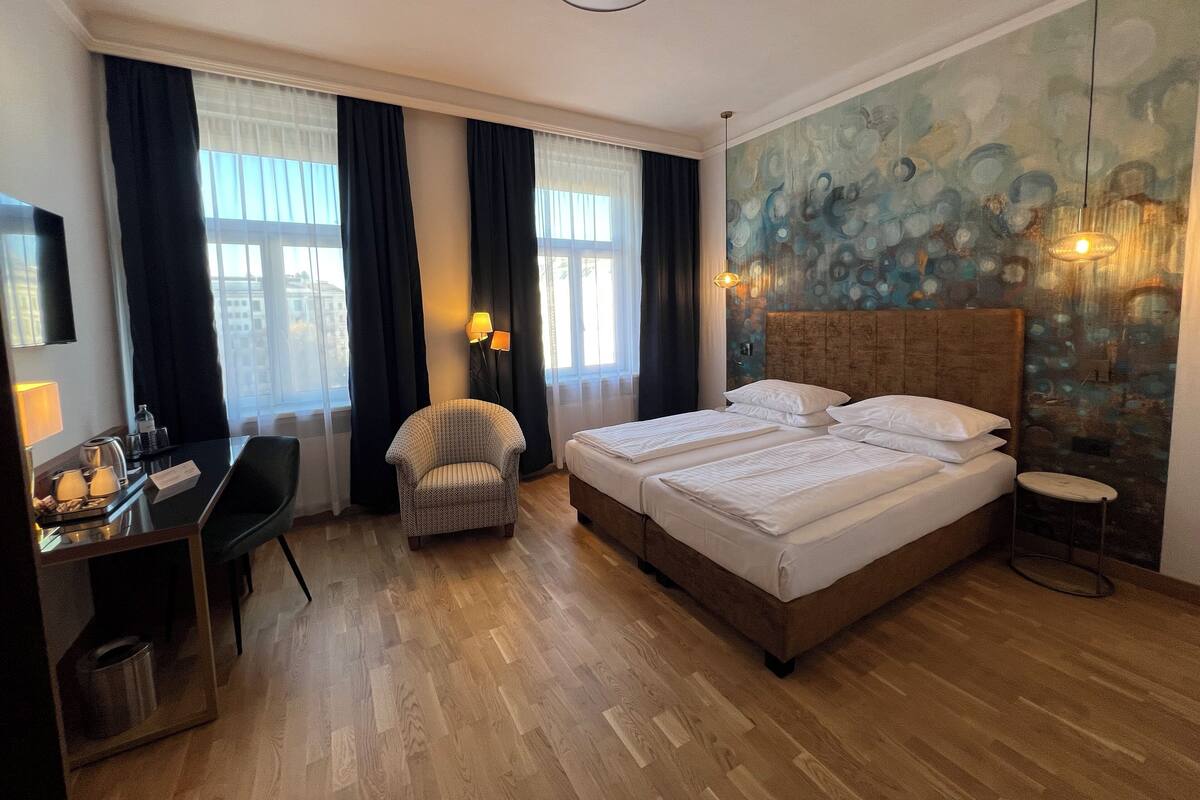 A hotel room with a large bed, a desk with a chair, a small armchair, and a wall-mounted TV.