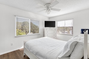 A bedroom with a bed, a dresser, a TV, and two windows with blinds. - Beachfront-Great for Groups-Privacy-Pets (Indian Rocks Beach)