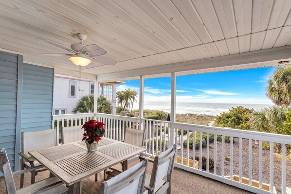 A covered patio with a table and chairs, overlooking a beach.