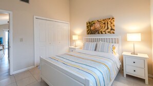 A bedroom with a bed, two bedside tables, a nightstand, a door, and a wall-mounted artwork. - Oceanfront Home | Pets Welcome (Indian Rocks Beach)