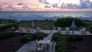 A deck with outdoor seating and a view of the ocean at sunset. - Oceanfront Home | Pets Welcome (Indian Rocks Beach)