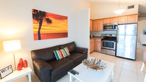 A modern living room with a leather sofa, a coffee table, and a painting of a sunset. - Oceanfront Home | Pets Welcome (Indian Rocks Beach)