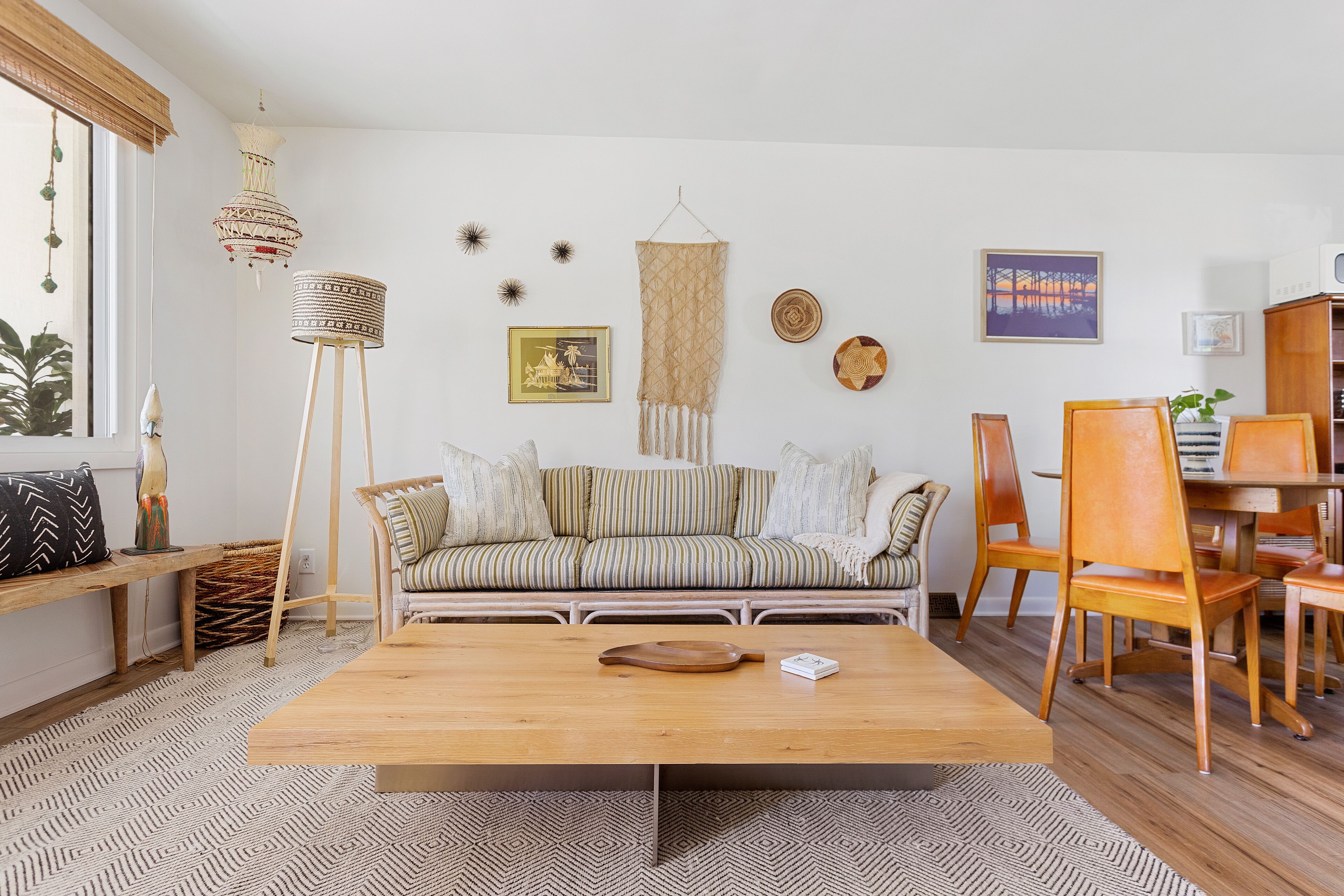 Una sala de estar con una mesa de centro de madera, sofá a rayas y un comedor con sillas y mesa de madera.