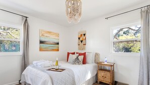 A bedroom with a bed, a bedside table, a wall art piece, and a window with curtains.