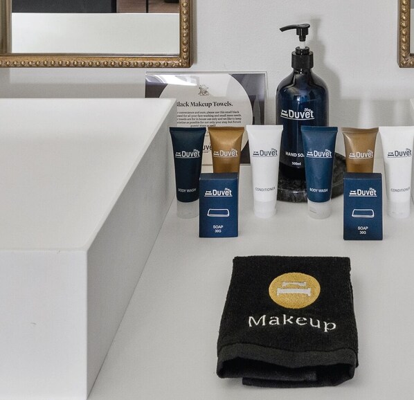 A bathroom vanity with a black makeup towel, a bottle of DuVet hand soap, and various DuVet body wash and conditioner bottles.