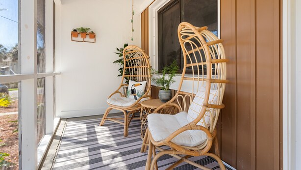 A porch with wicker chairs and a table, a potted plant, and a hanging light fixture.