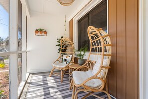 A porch with wicker chairs and a table, a potted plant, and a hanging light fixture.