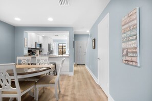 Una cocina moderna con armarios blancos, un microondas y un comedor con mesa y sillas de madera.