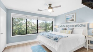 A bedroom with a large window, a ceiling fan, a bed with white bedding, and a nightstand with a lamp. - Golf Cart! | Lakefront Villa at Sandestin – On The Rocks ☀️ (Destin)