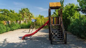 Ein Spielplatz mit einer Holzrutsche und Treppen, umgeben von Grünflächen und blauem Himmel.