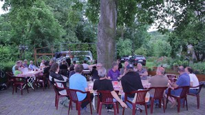A group of people seated at round tables outdoors, surrounded by greenery and trees. - Gasthof Linde-Classico (Bad Mergentheim)