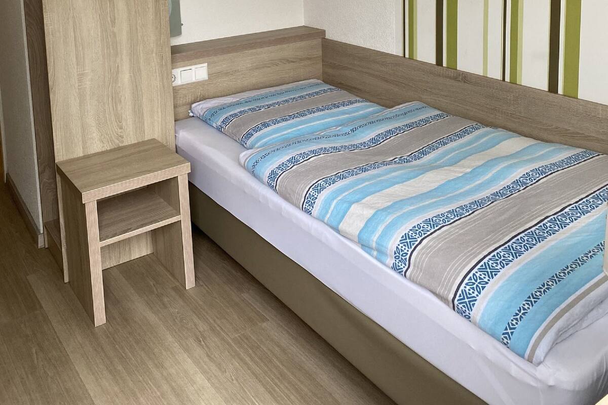 A single bed with a striped bedspread, a wooden nightstand, and a vertical striped wall.