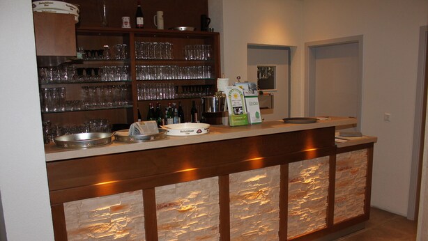 A bar area with a stone facade, shelves with glasses, and various bottles. - Gasthof Linde-Classico (Bad Mergentheim)