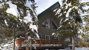 A modern building with a wooden deck, surrounded by snow-covered trees. - Cozy Cabin with Hot Tub Near Yellowstone (Island Park)