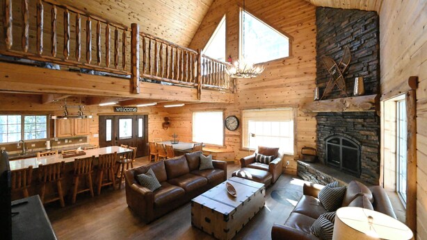 A spacious log cabin interior with a dining area, living room, and a stone fireplace. - Cozy Cabin with Hot Tub Near Yellowstone (Island Park)