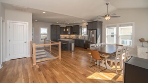 A spacious kitchen with modern appliances, a dining area with a wooden table and chairs, and a staircase leading to an upper level. - A magical setting with ocean and marsh views! (Oak Island)