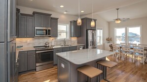 A modern kitchen with grey cabinets, stainless steel appliances, and a large island with bar stools. - A magical setting with ocean and marsh views! (Oak Island)