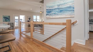 A spacious living area with a wooden staircase, a dining table, and a large abstract painting on the wall. - A magical setting with ocean and marsh views! (Oak Island)