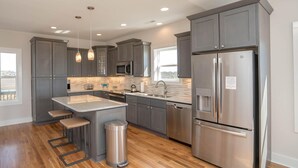 A modern kitchen with grey cabinets, stainless steel appliances, and a central island with stools. - A magical setting with ocean and marsh views! (Oak Island)