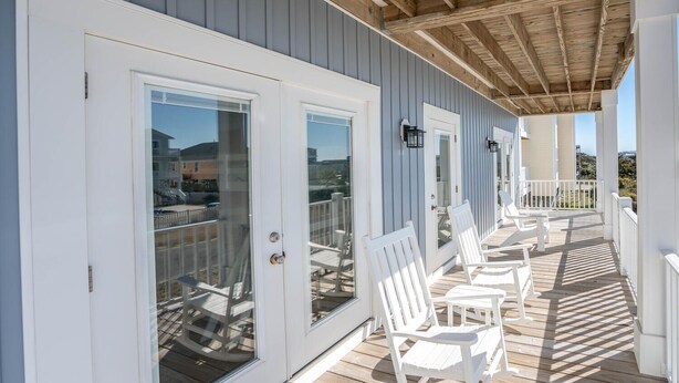 A covered deck with white chairs and a railing, overlooking a residential area. - A magical setting with ocean and marsh views! (Oak Island)