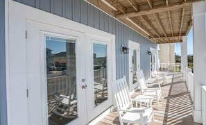 A covered deck with white chairs and a railing, overlooking a residential area. - A magical setting with ocean and marsh views! (Oak Island)