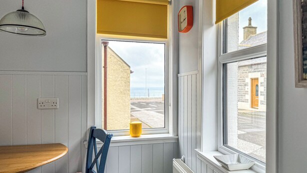 A room with a window, a chair, a table, a yellow cup, and a clock on the wall. - Three Creeks Cottage (Portknockie)