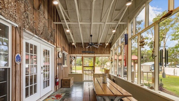 A covered patio with wooden benches and a ceiling fan, large windows, and a view of the outdoors. - Cypress Crab House of Steinhatchee! 1 block to river, parking, porch, parking (Steinhatchee)