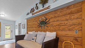 A cozy living room with a wooden accent wall, a decorative crab, and a sign above it. - Cypress Crab House of Steinhatchee! 1 block to river, parking, porch, parking (Steinhatchee)