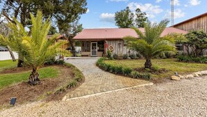 A rustic building with a red roof, surrounded by palm trees and a gravel pathway leading to the entrance. - Cypress Crab House of Steinhatchee! 1 block to river, parking, porch, parking (Steinhatchee)