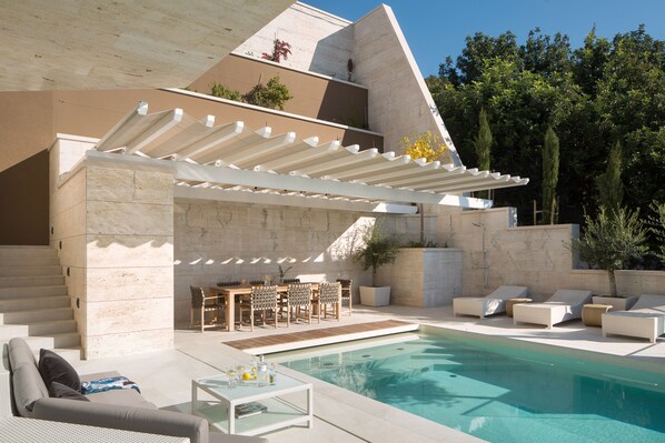 A modern outdoor pool area with a pergola, seating, and a staircase leading to an upper level.
