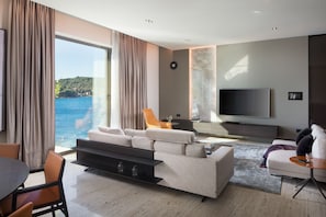 Een moderne woonkamer met een grote televisie, comfortabele zitplaatsen, een eethoek en uitzicht op zee.