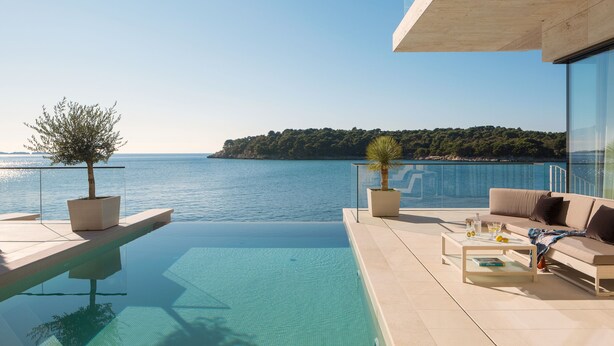 A modern outdoor terrace with a pool, a sofa, and a table, overlooking a clear blue sea and a forested island. - New Villa, Comfort & Luxury, Beachfront, Prestigious Location, Full experience (Dubrovnik)