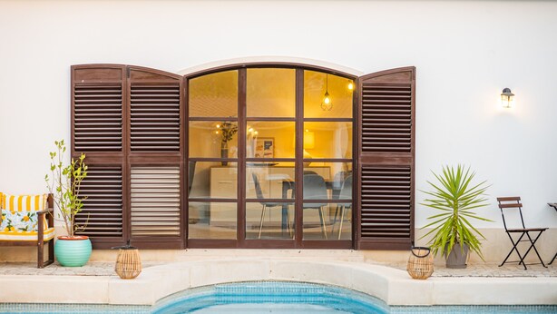 A poolside area with a large window, potted plants, and outdoor furniture.