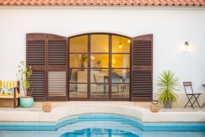 A poolside area with a large window, potted plants, and outdoor furniture. - Quinta do Quartel - Évora (Évora)