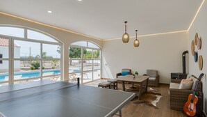 A spacious living area with a ping pong table, seating, and a view of a swimming pool.