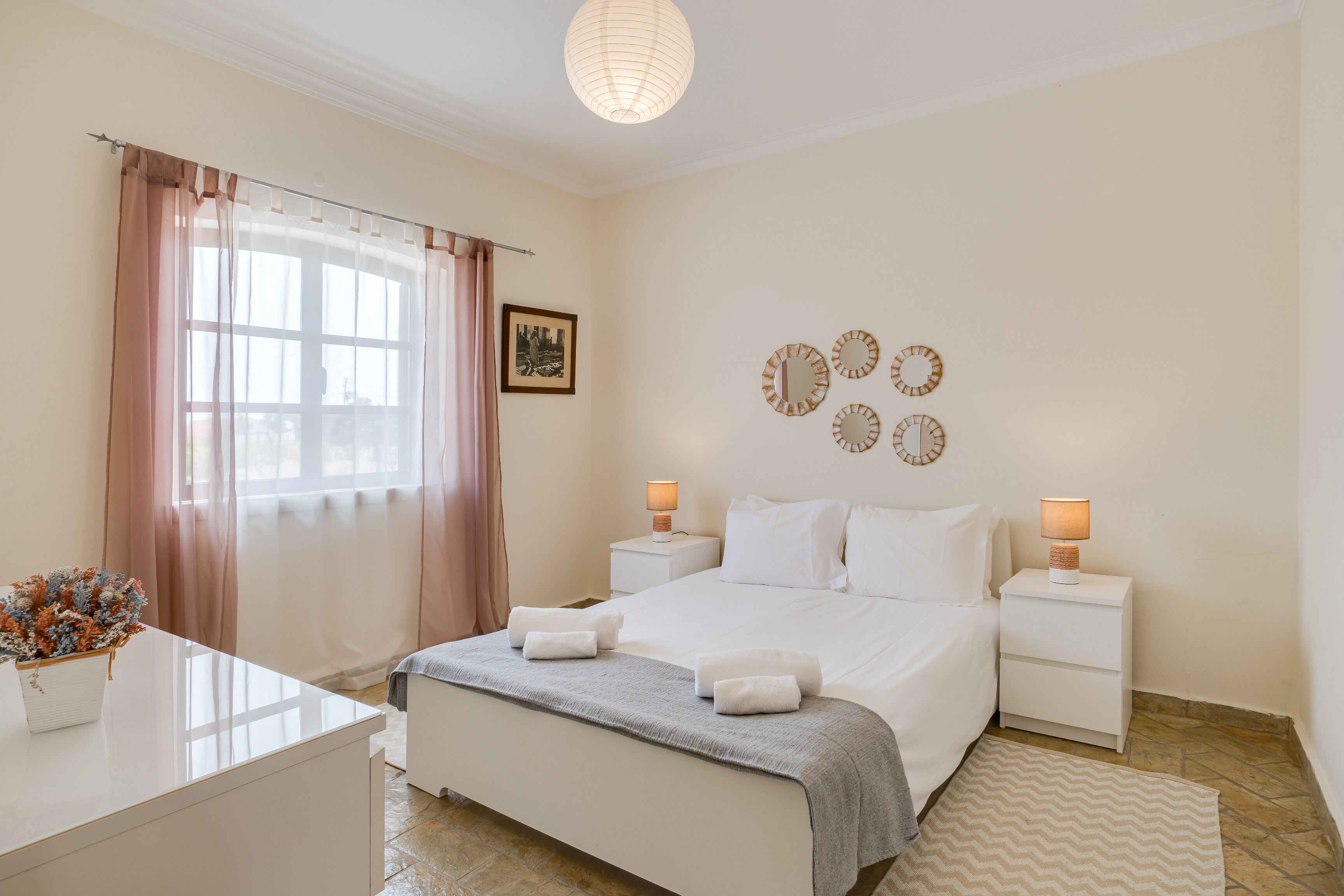 Une chambre à coucher bien rangée, avec un lit, des tables de chevet, une lampe, un tableau au mur et une horloge décorative.