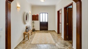 A hallway with a wooden archway, a bench, a potted plant, a rug, and a door with a window.