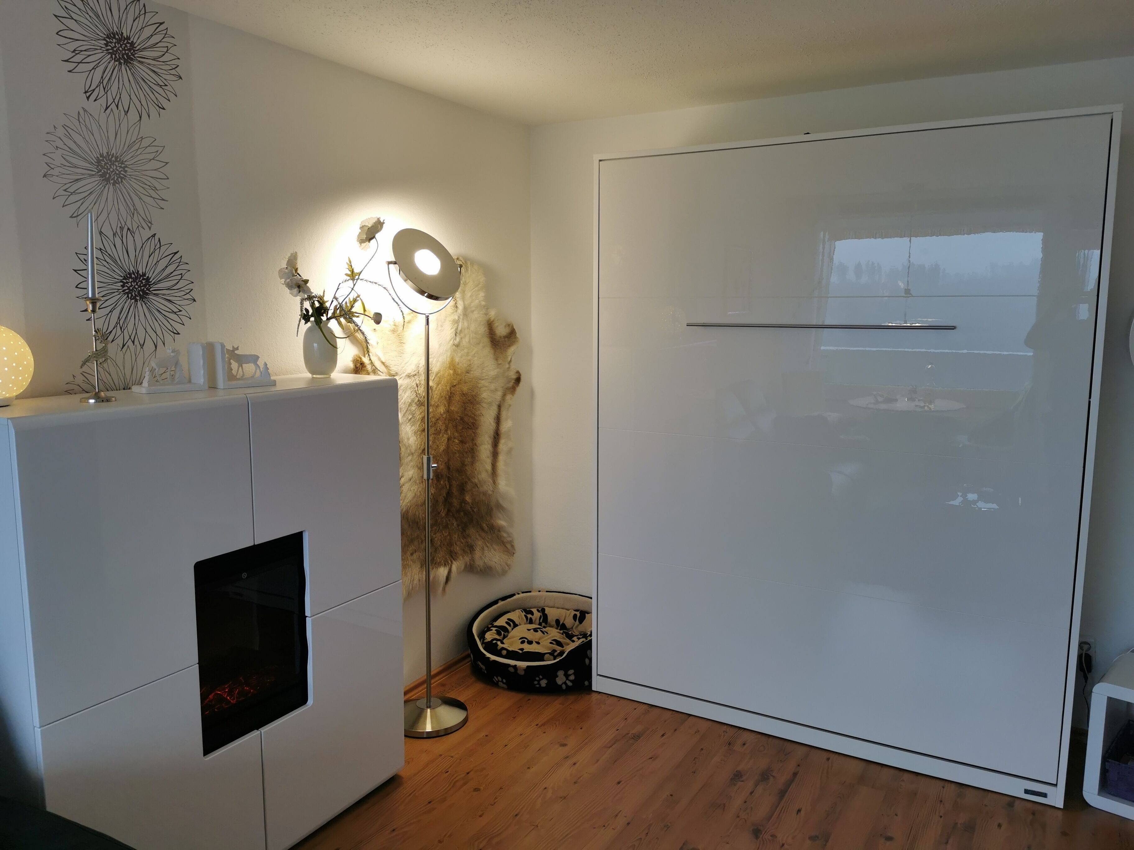 A modern room with a white wardrobe, a floor lamp, a decorative wall piece, and a fur rug.