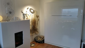 Ein modernes Zimmer mit einem weißen Kleiderschrank, einer Stehlampe, einer Wanddekoration und einem Fellteppich.