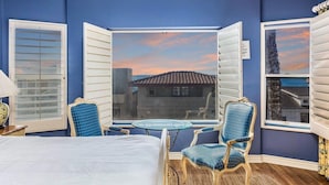 Une chambre à coucher comprenant un lit, deux chaises, une petite table et une grande fenêtre avec des volets.