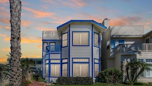 Une maison moderne à deux étages, avec une façade bleue et blanche, un balcon et une pelouse bien entretenue.